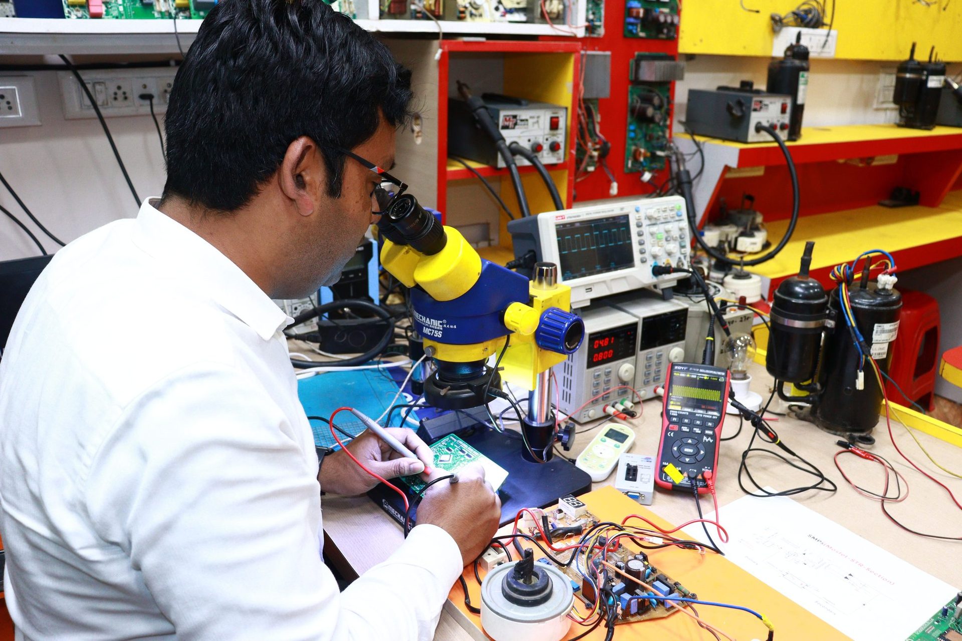 Engineer testing a circuit board with an oscilloscope and microscope